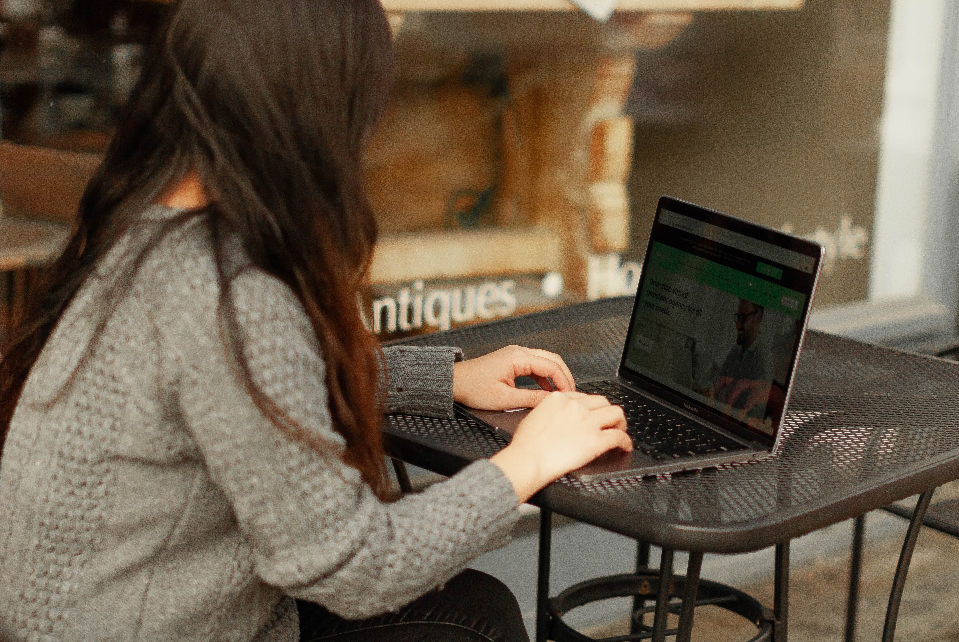 An entrepreneur working on a laptop at an outdoor café table, viewing a virtual assistant agency website