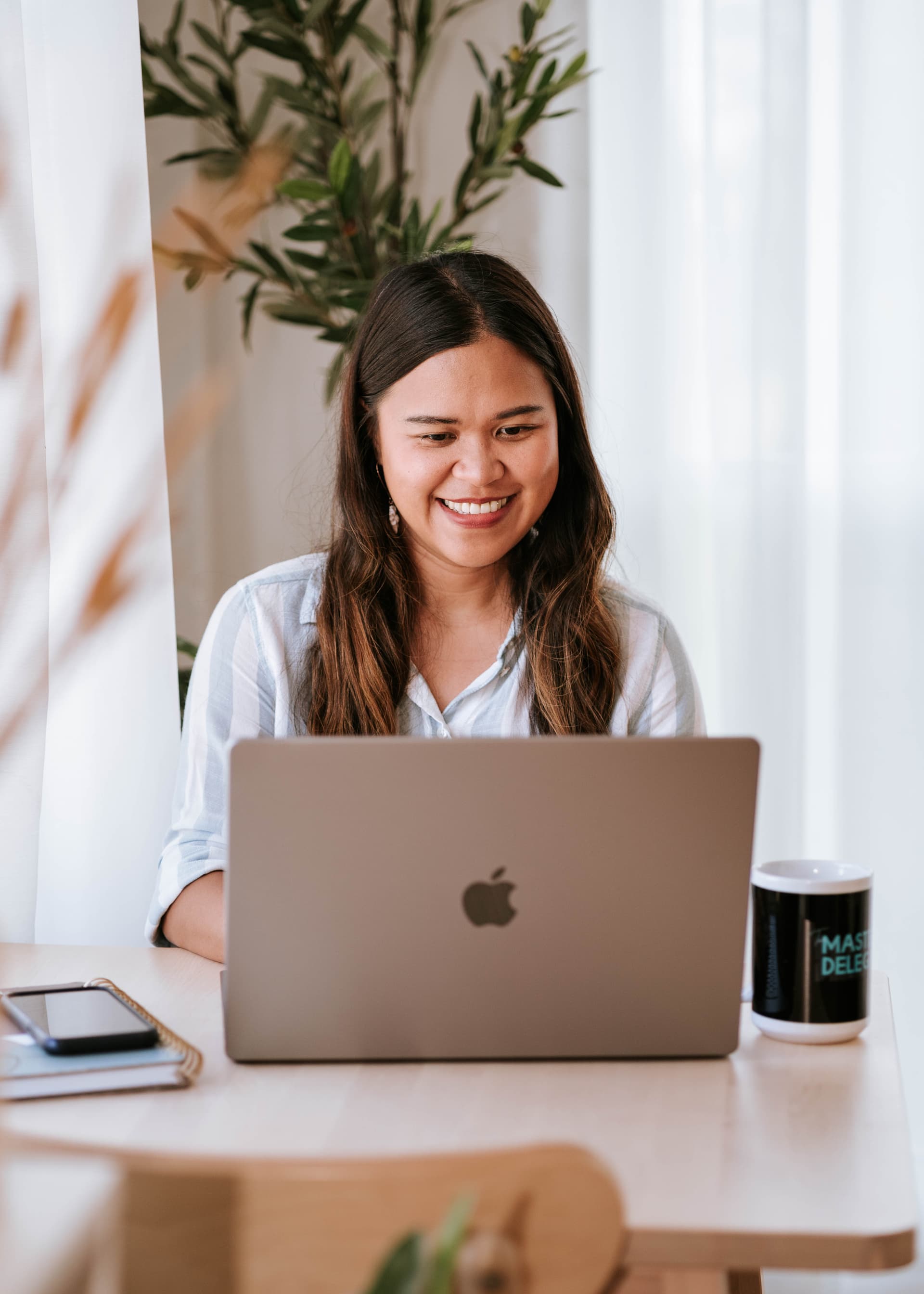 Kristy Yoder smiling while working on her laptop at a sunlit desk