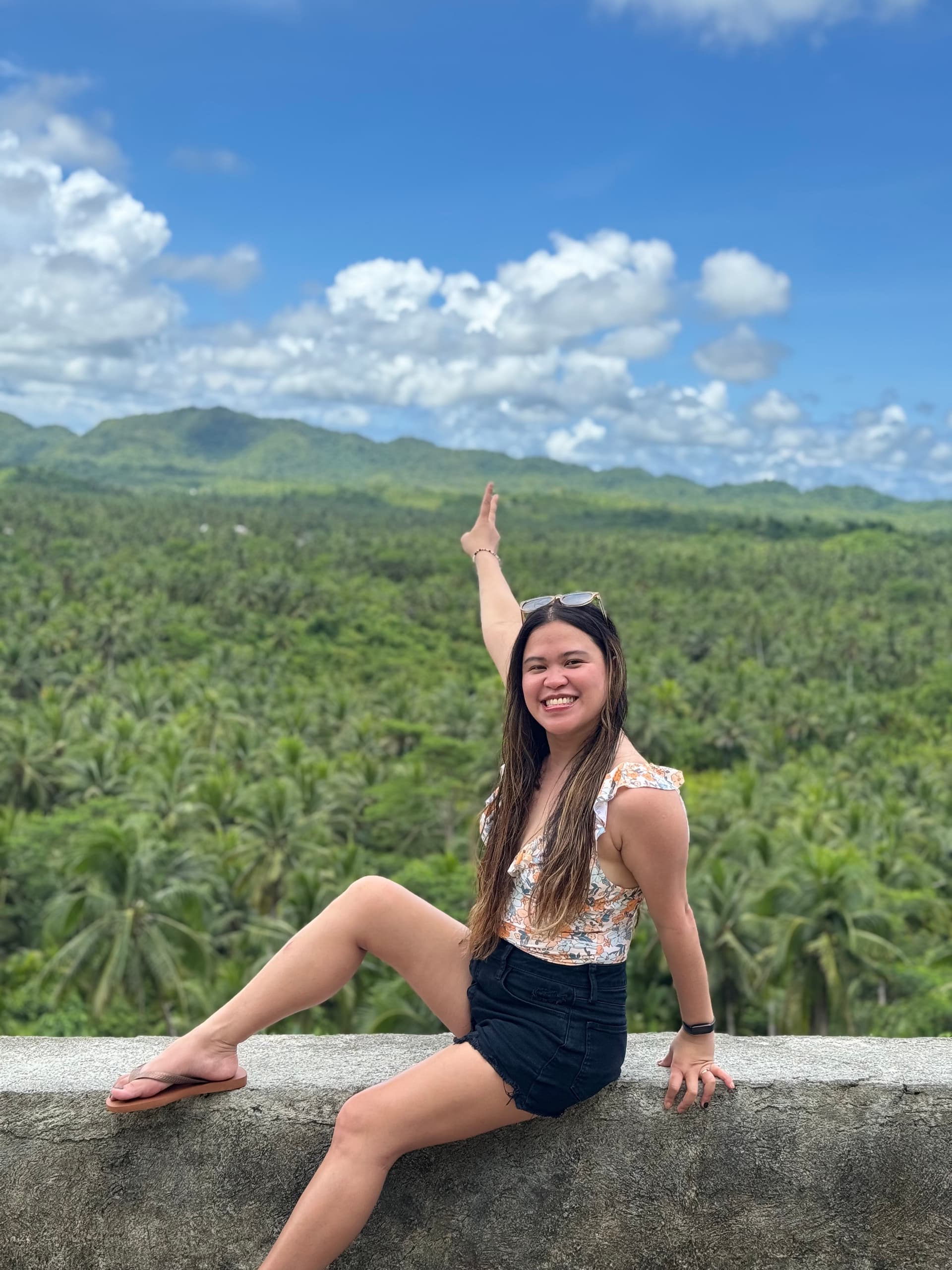 Kristy Yoder smiling and raising her arm in celebration on a hillside overlooking palm forests and mountains, reflecting a life of freedom, joy, and balance beyond work